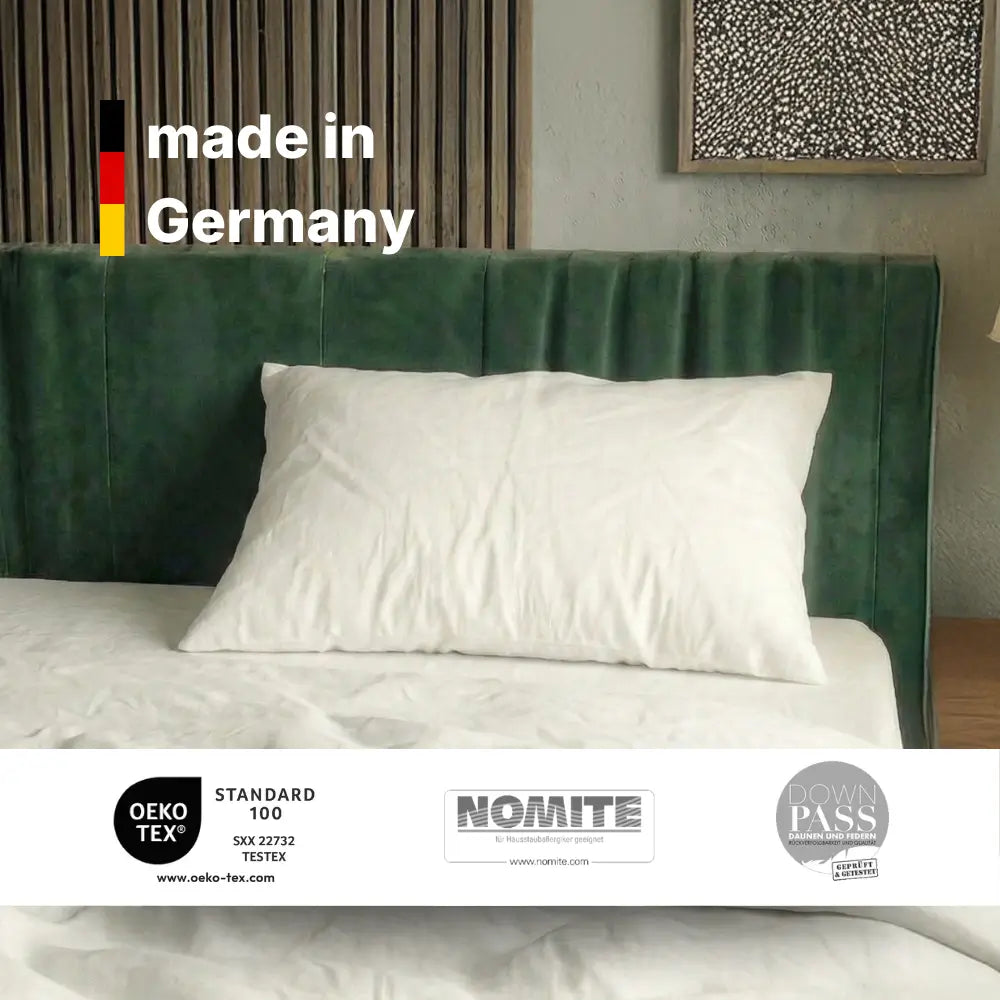 Weißes Essential Federkissen auf einem Bett mit Hinweis ‚made in Germany‘ und eingeblendeten Zertifikatslogos.