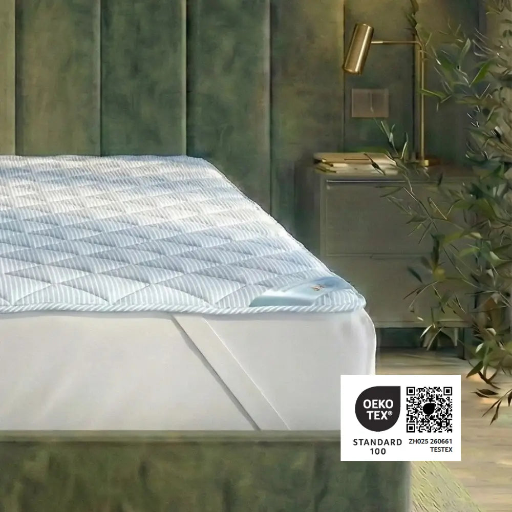 TopCool Matratzenauflage mit gestreiftem Bezug auf dem Bett, zertifiziert nach OEKO-TEX® Standard 100 für geprüfte Materialqualität und Hautverträglichkeit