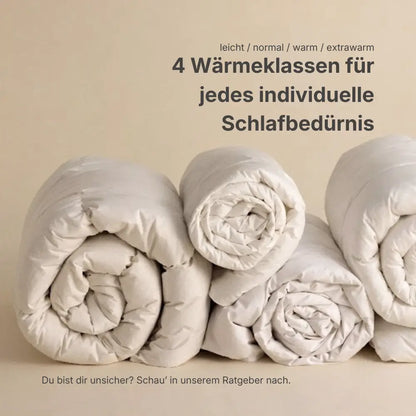 Mehrere zusammengerollte Bettdecken nebeneinander, die vier Wärmeklassen von leicht über normal und warm bis extrawarm symbolisieren, passend für unterschiedliche individuelle Schlafbedürfnisse