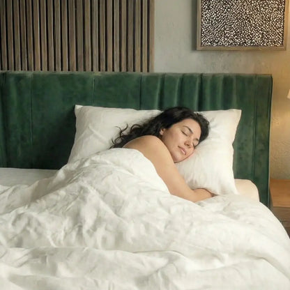 Schlafende Person liegt seitlich auf einem weißen Essential Federkissen in einem Bett mit grünem Kopfteil.