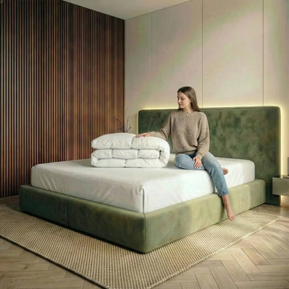 Frau sitzt auf einem modernen Bett und berührt eine gefaltete weiße Superior Daunendecke mit hochwertiger Steppung, präsentiert für luxuriösen Schlafkomfort