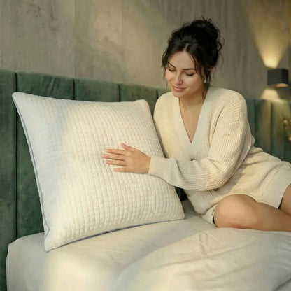 Frau sitzt auf einem Bett und berührt das weiße Essential Kühlkissen mit strukturierter Oberfläche vor grünem Kopfteil