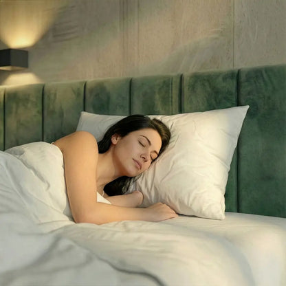 Schlafende Person liegt seitlich auf einem weißen Premium Feder- und Daunenkissen in einem Bett mit grünem Kopfteil.