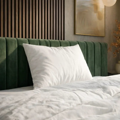 Weißes Essential Federkissen mit glattem Bezug auf einem Bett mit grünem, gepolstertem Kopfteil.