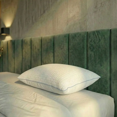 Weißes Essential Kühlkissen mit strukturierter Oberfläche liegt flach auf einem Bett vor grünem Kopfteil